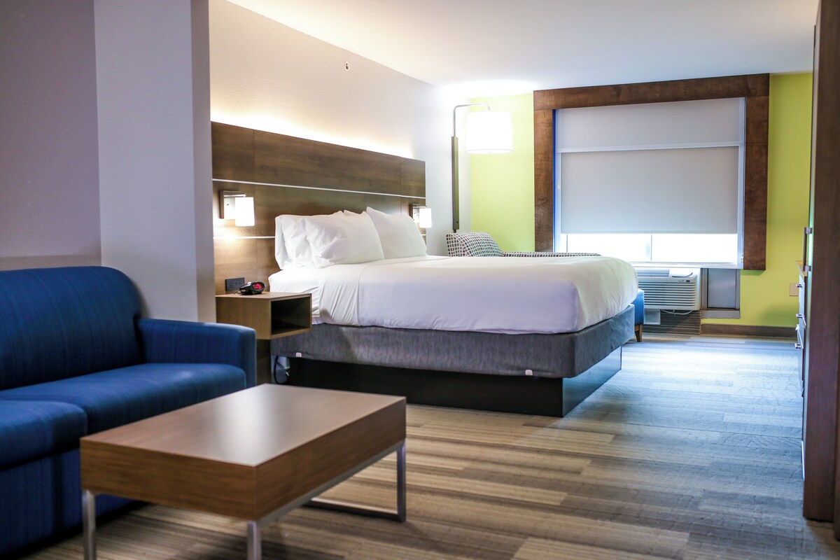 A hotel room with a bed, a blue sofa, a wooden coffee table, a nightstand, and a lamp.