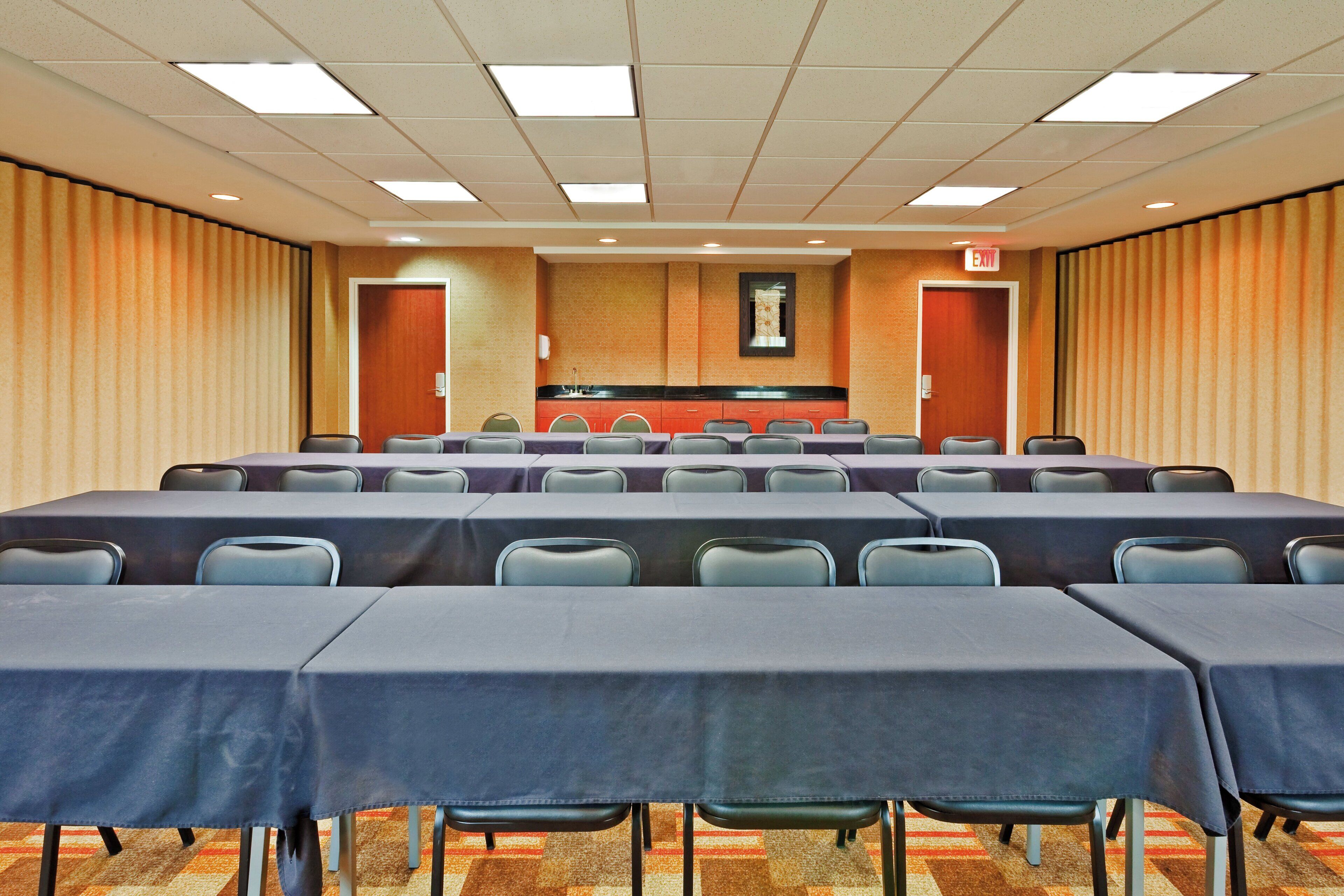 A conference room with multiple tables and chairs, a podium, and an exit sign.