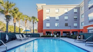 A swimming pool with lounge chairs and palm trees, surrounded by a building with multiple windows and a brick facade. - Holiday Inn Express Hotel & Suites Ocoee East by IHG (Orlando)