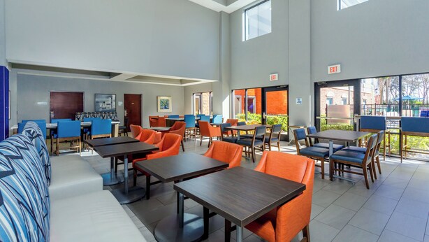 A spacious indoor area with multiple tables and chairs, a sofa, and a door marked "EXIT". - Holiday Inn Express Hotel & Suites Ocoee East by IHG (Orlando)