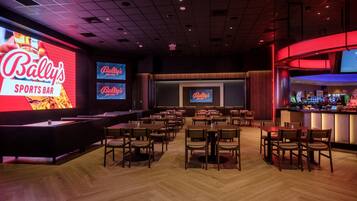 Eine Sportsbar mit mehreren Bildschirmen, die 'Bally's Quad Cities' zeigen, sowie ein Barbereich mit Hockern und einer Theke.