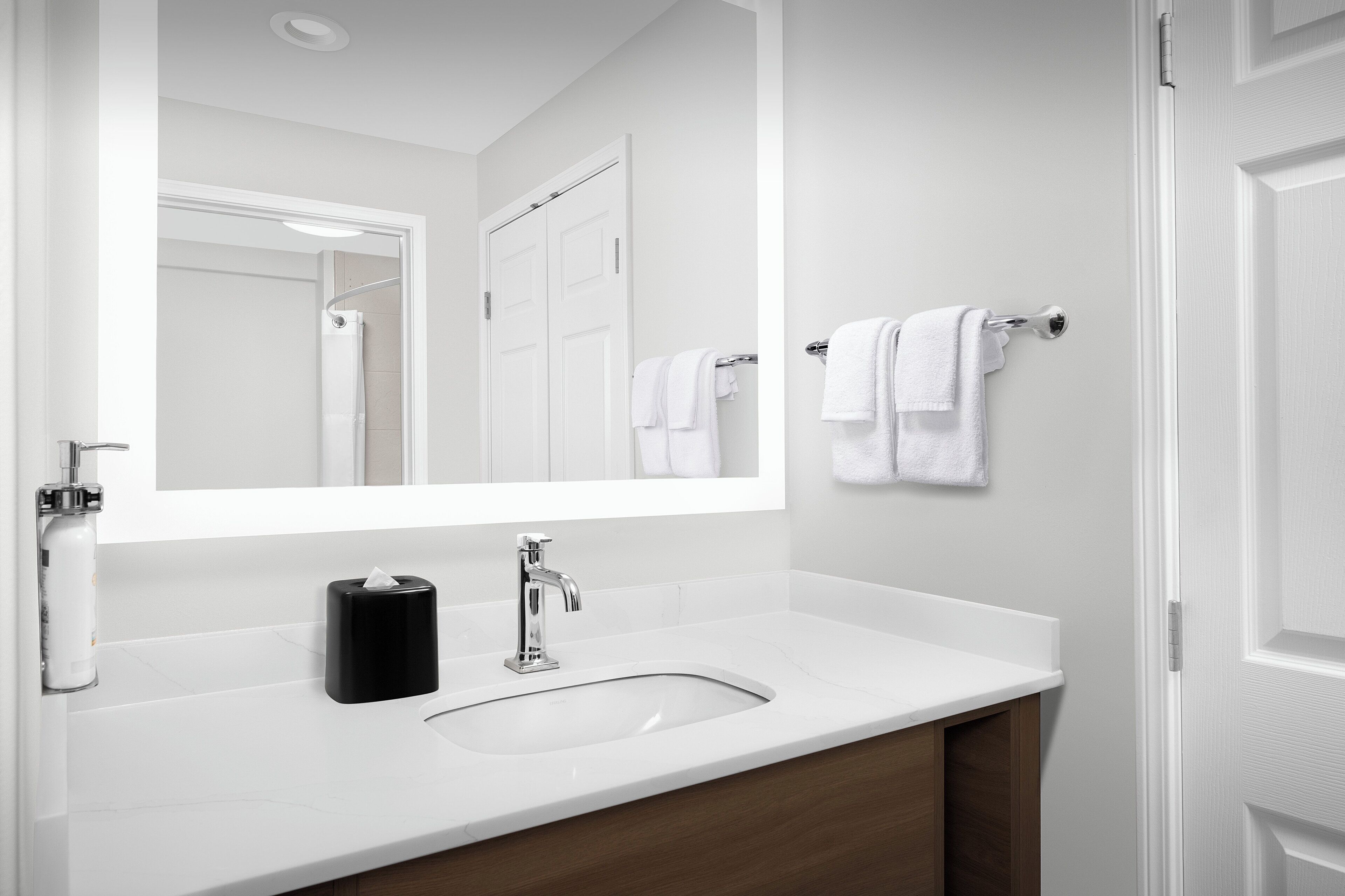 A modern bathroom with a white sink, a large mirror, and a towel rack.