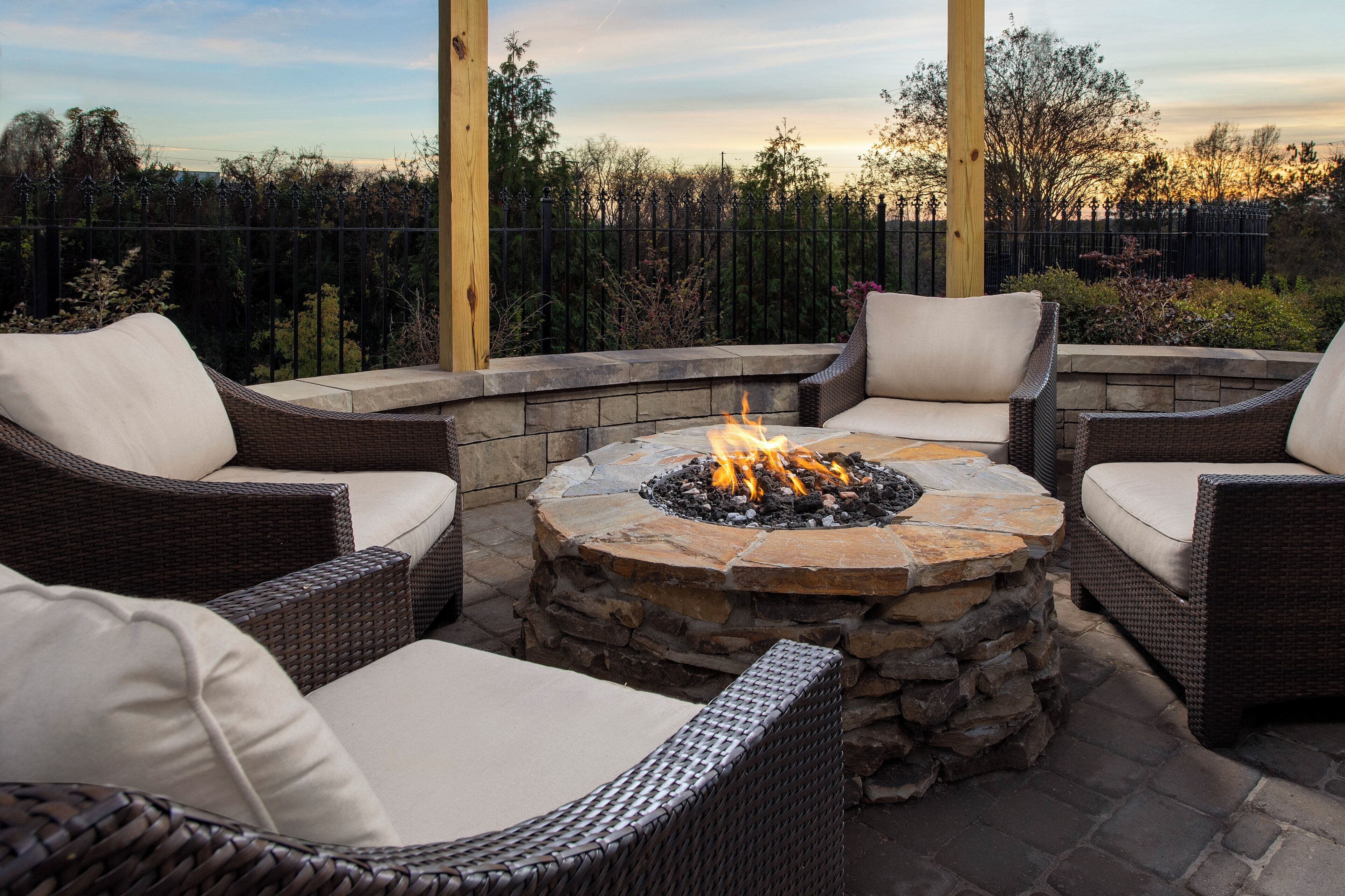 A fire pit surrounded by wicker furniture with cushions, set on a stone platform.
