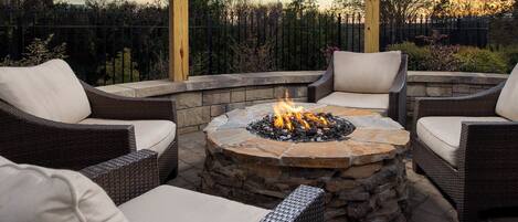 A fire pit surrounded by wicker furniture with cushions, set on a stone platform.
