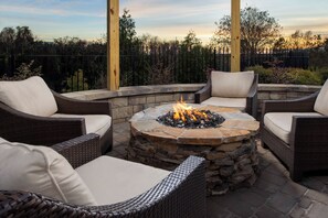 A fire pit surrounded by wicker furniture with cushions, set on a stone platform. - Staybridge Suites Columbia by IHG (Columbia)