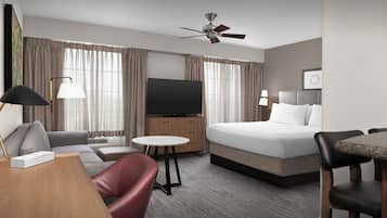 A hotel room with a bed, a TV, a desk with a lamp, a chair, and a small table.