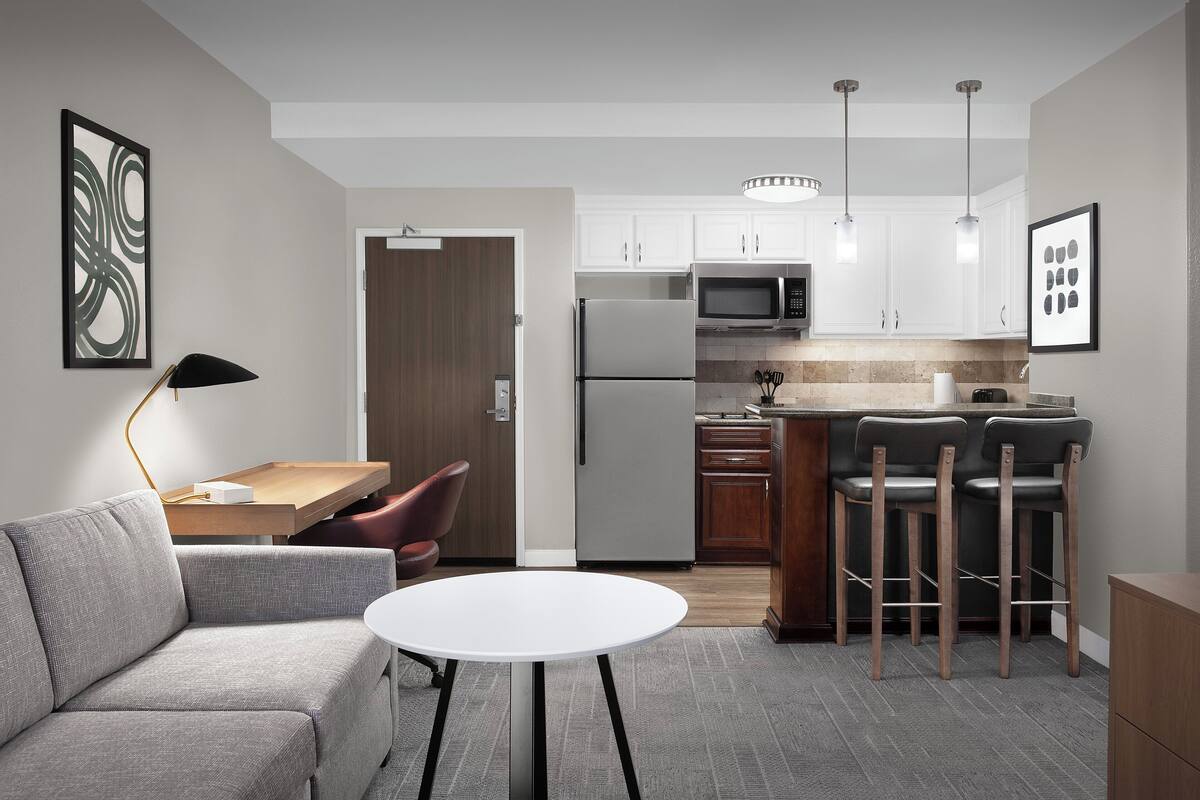 Una cocina moderna con armarios blancos, un refrigerador, un microondas y un comedor con un sofá y una pequeña mesa.