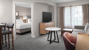 A hotel room with a bed, a TV, a desk, a chair, a sofa, and a window with curtains. - Staybridge Suites Columbia by IHG (Columbia)