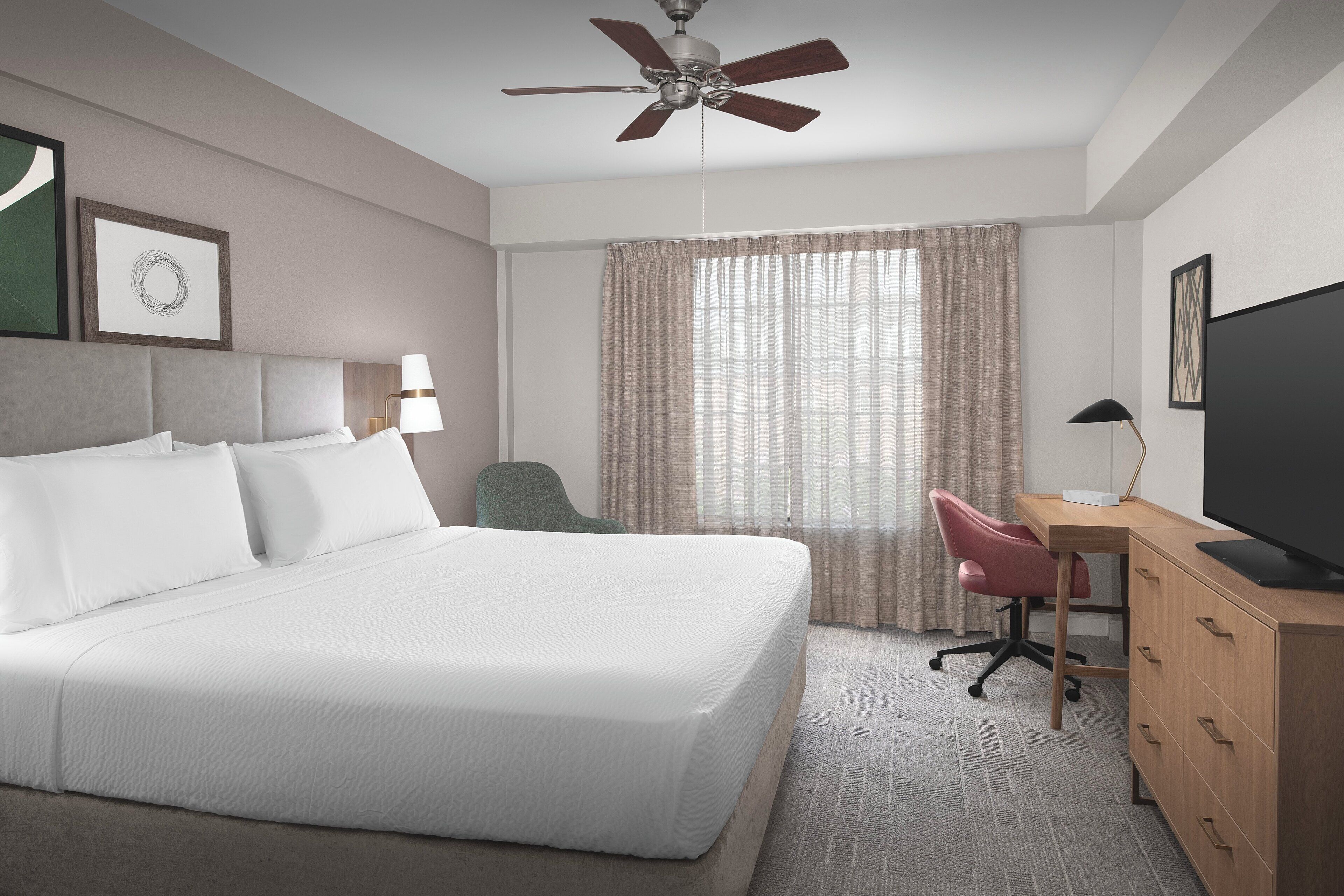 A hotel room with a bed, desk, chair, television, and curtains.
