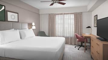 A hotel room with a bed, desk, chair, television, and curtains.