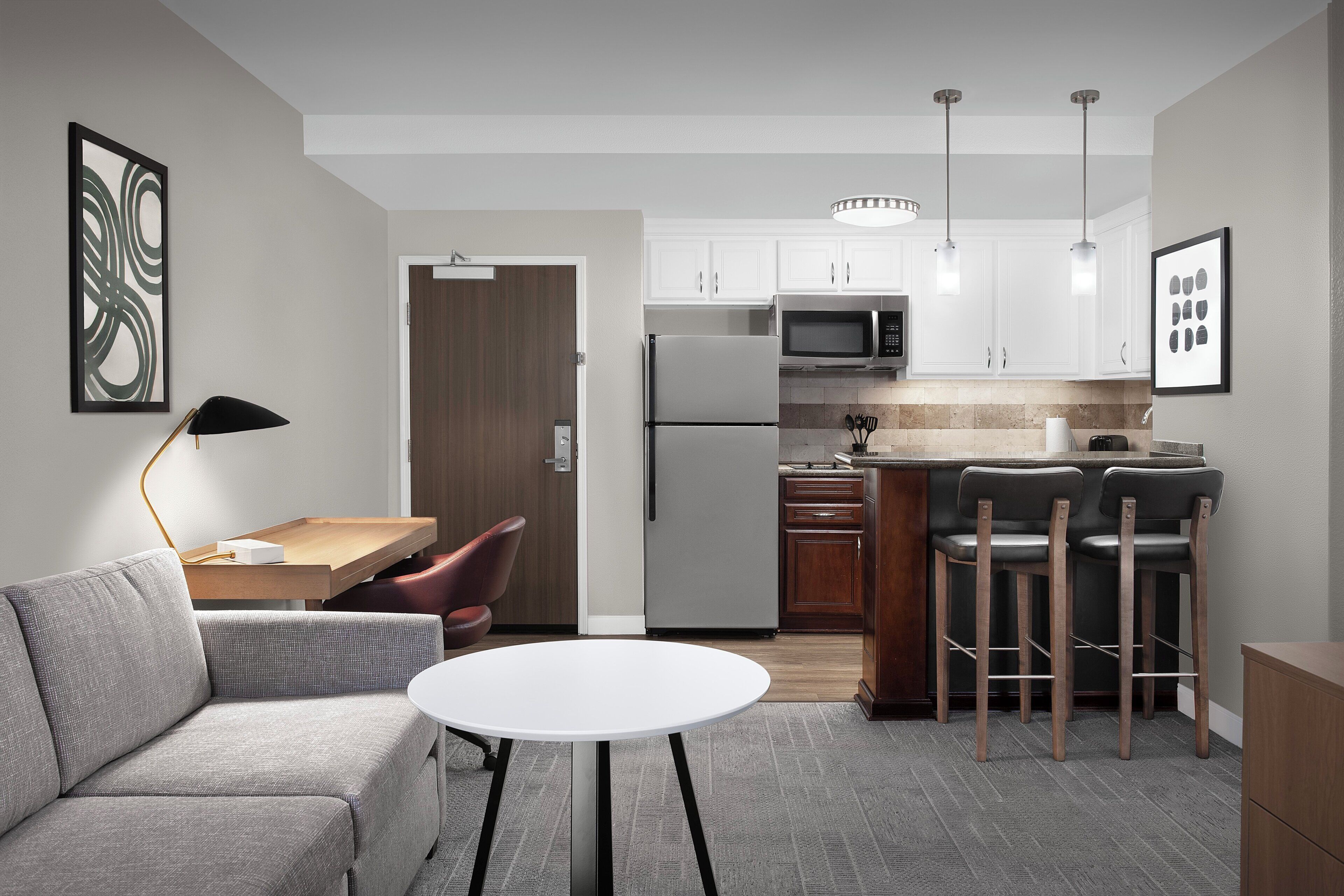 A modern kitchen with white cabinets, a stainless steel refrigerator, a microwave, and a bar area with stools.