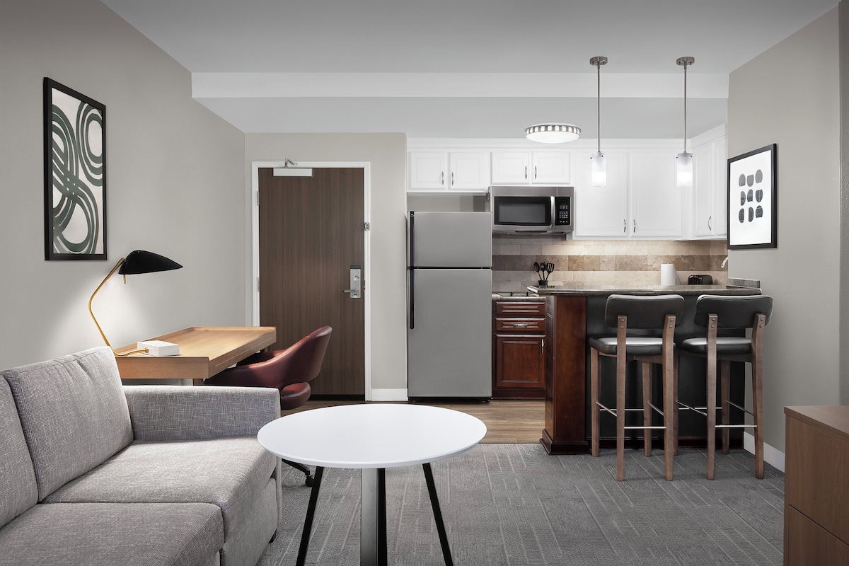 A modern kitchen with white cabinets, a refrigerator, a microwave, and a dining area with a sofa and a small table.