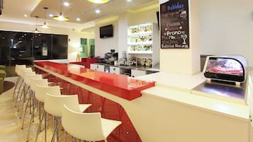 A bar area with a red counter, white stools, and a television screen.