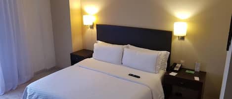 Una habitación de hotel con cama, dos mesitas de noche, una lámpara y un teléfono.