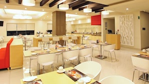 Uma sala de jantar moderna com várias mesas e cadeiras, uma cozinha ao fundo e um painel decorativo na parede.