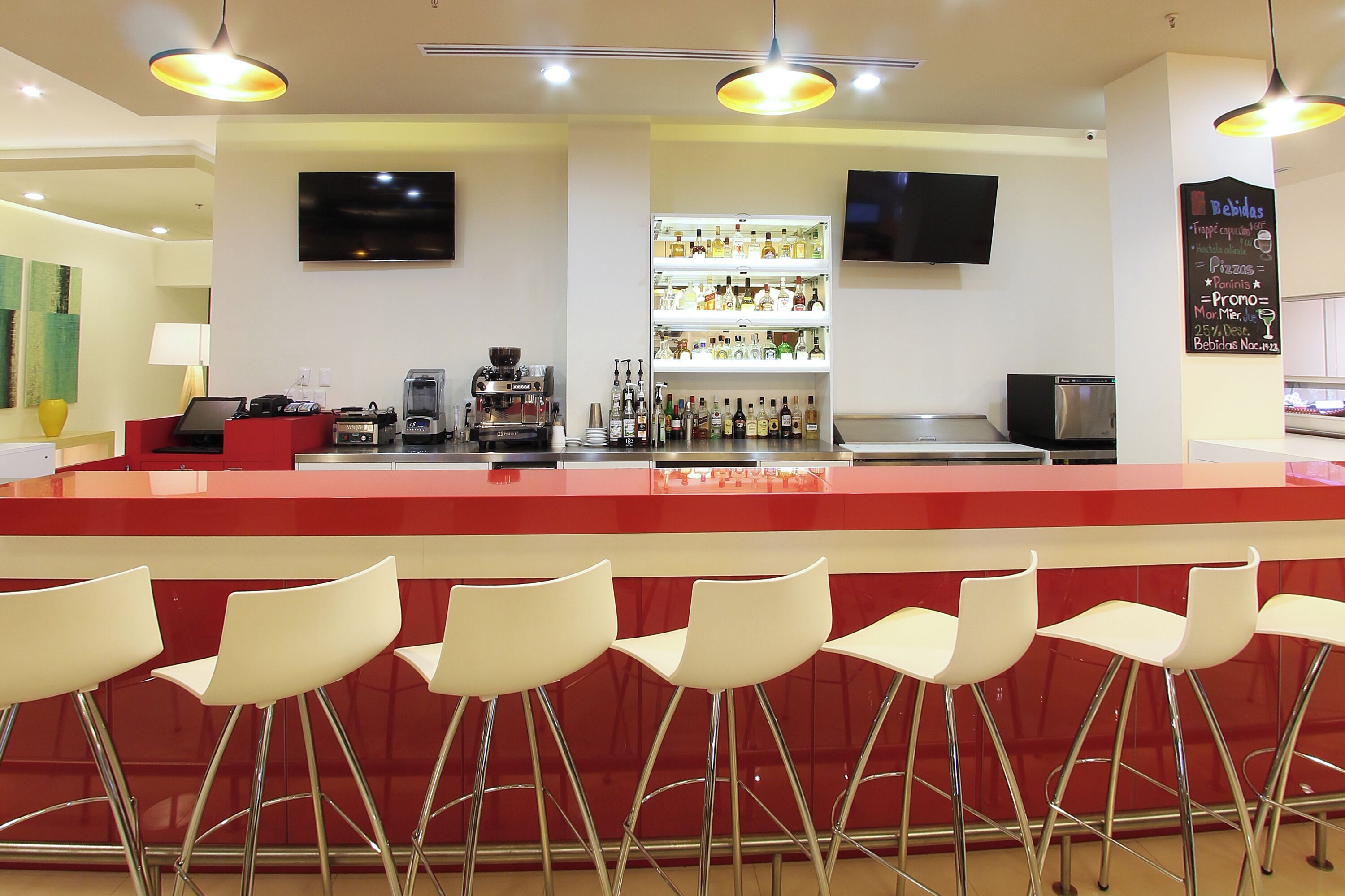 A bar area with a red counter, white bar stools, and a television mounted on the wall.