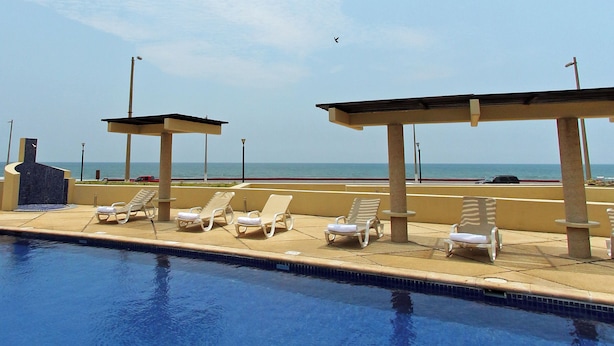 Uma área à beira da piscina com espreguiçadeiras e vista para o oceano.