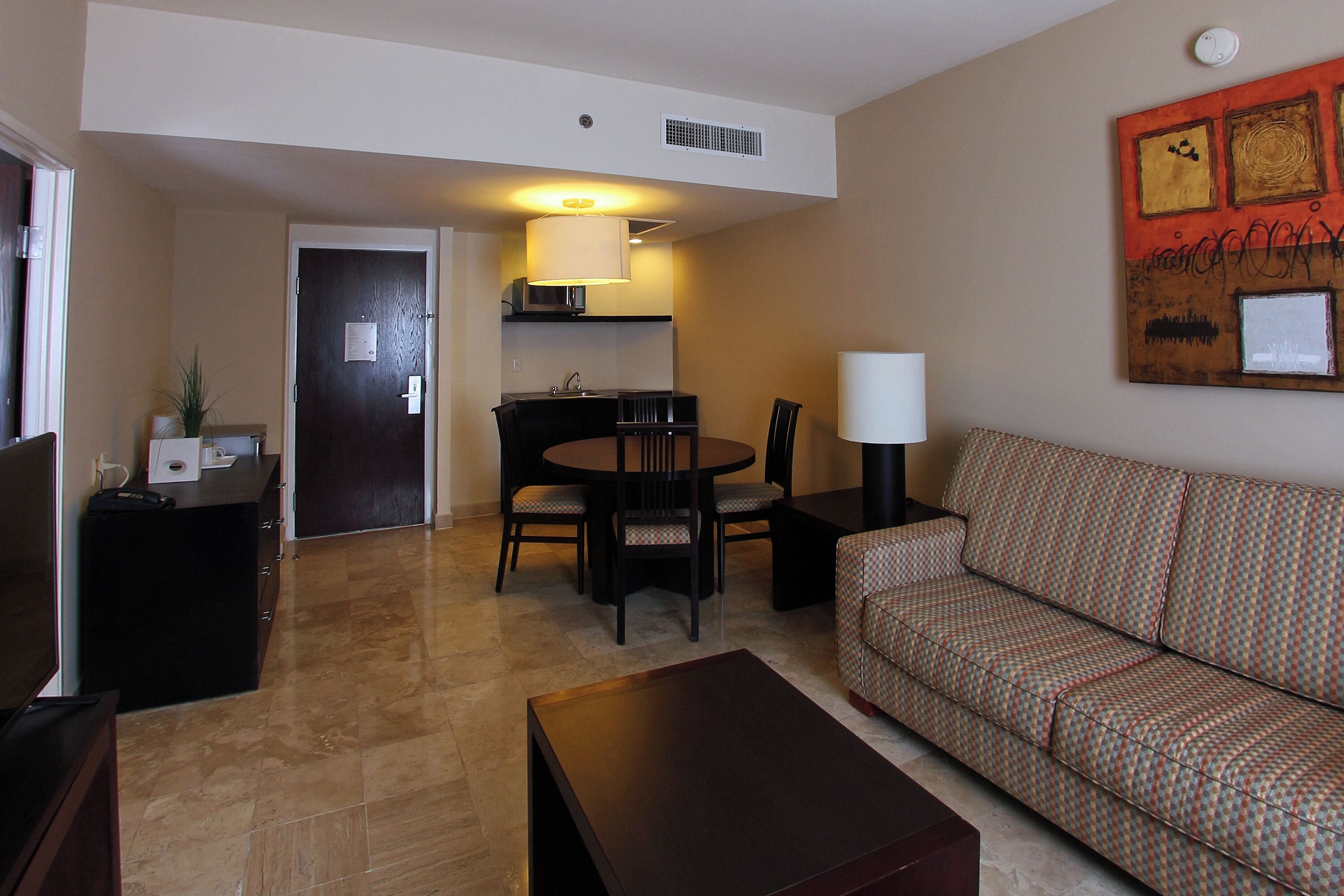 A living room with a sofa, a coffee table, a TV, a dining table with chairs, and a kitchen area with a microwave.