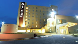 Um hotel com uma placa grande de 'Fiesta Inn', uma entrada ampla com fachada de vidro e exterior bem iluminado.