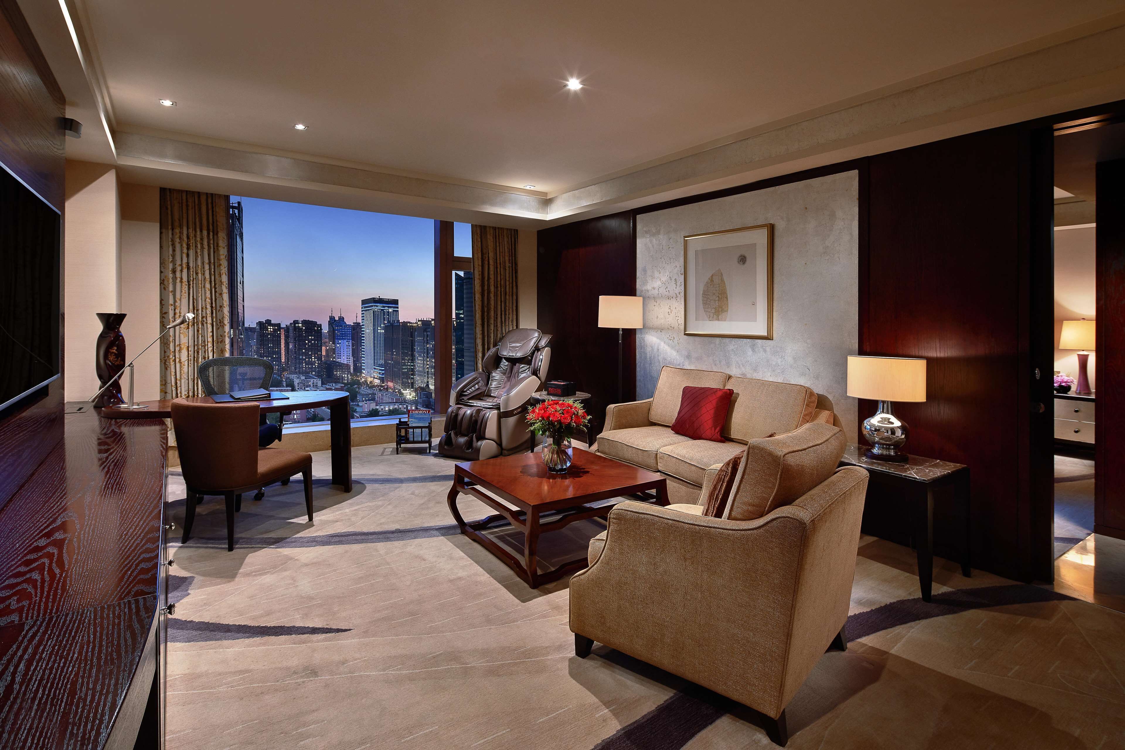 A modern hotel room with a city view, a leather sofa, a dining table, and a TV.