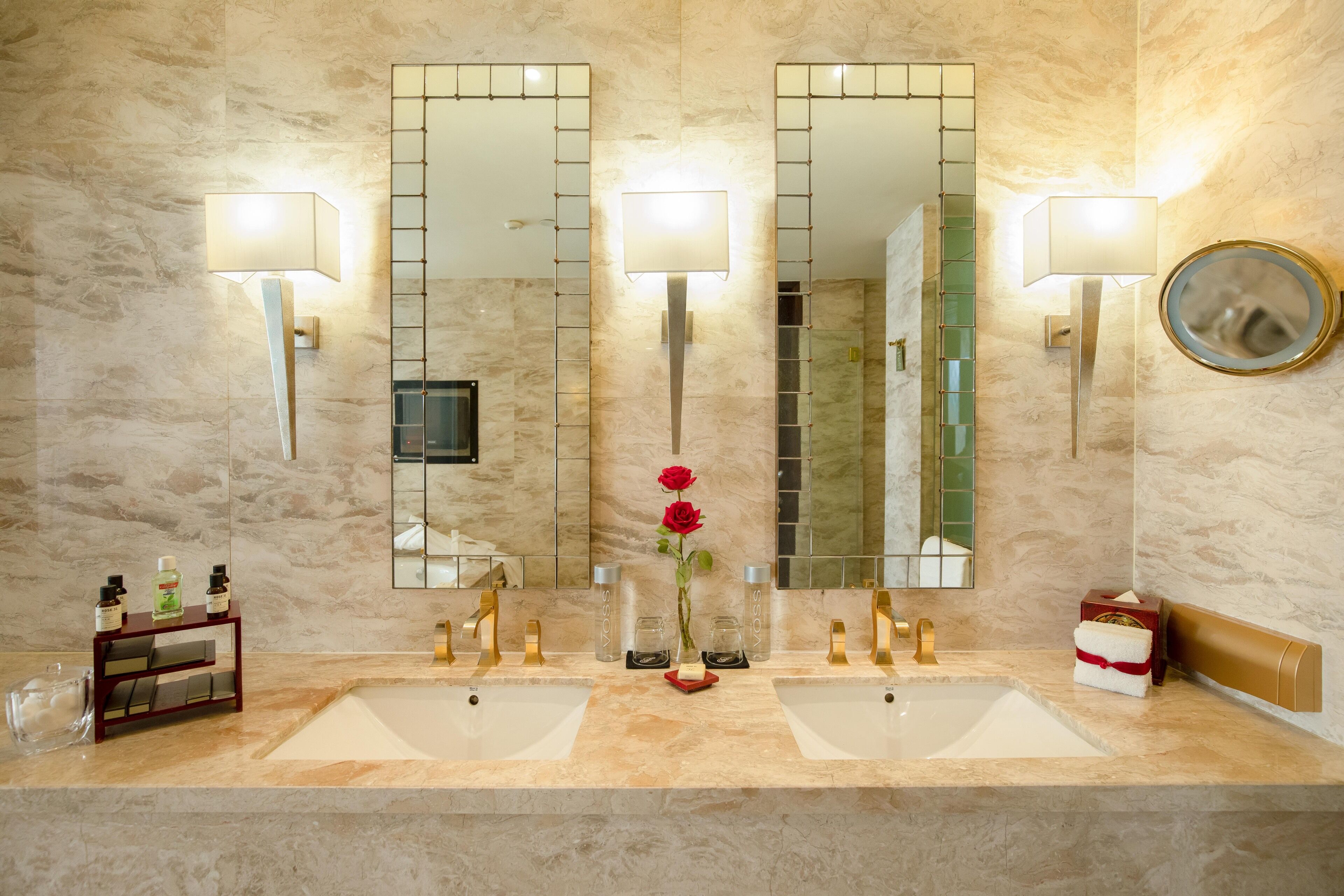 Un baño con dos lavamanos, un espejo y un florero con una rosa.