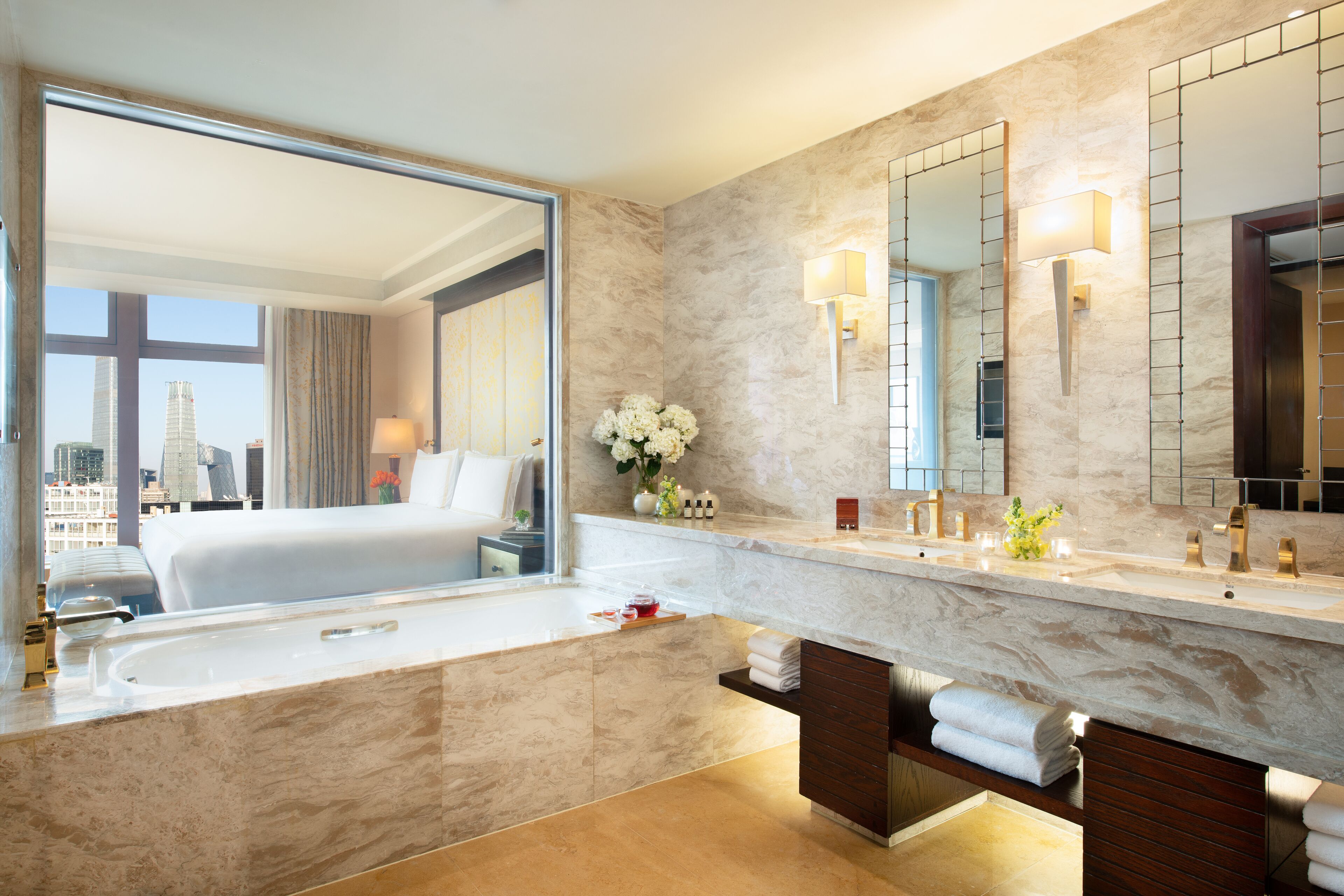 Un baño de hotel moderno con una bañera grande, un tocador con espejo y vistas a la ciudad por la ventana.