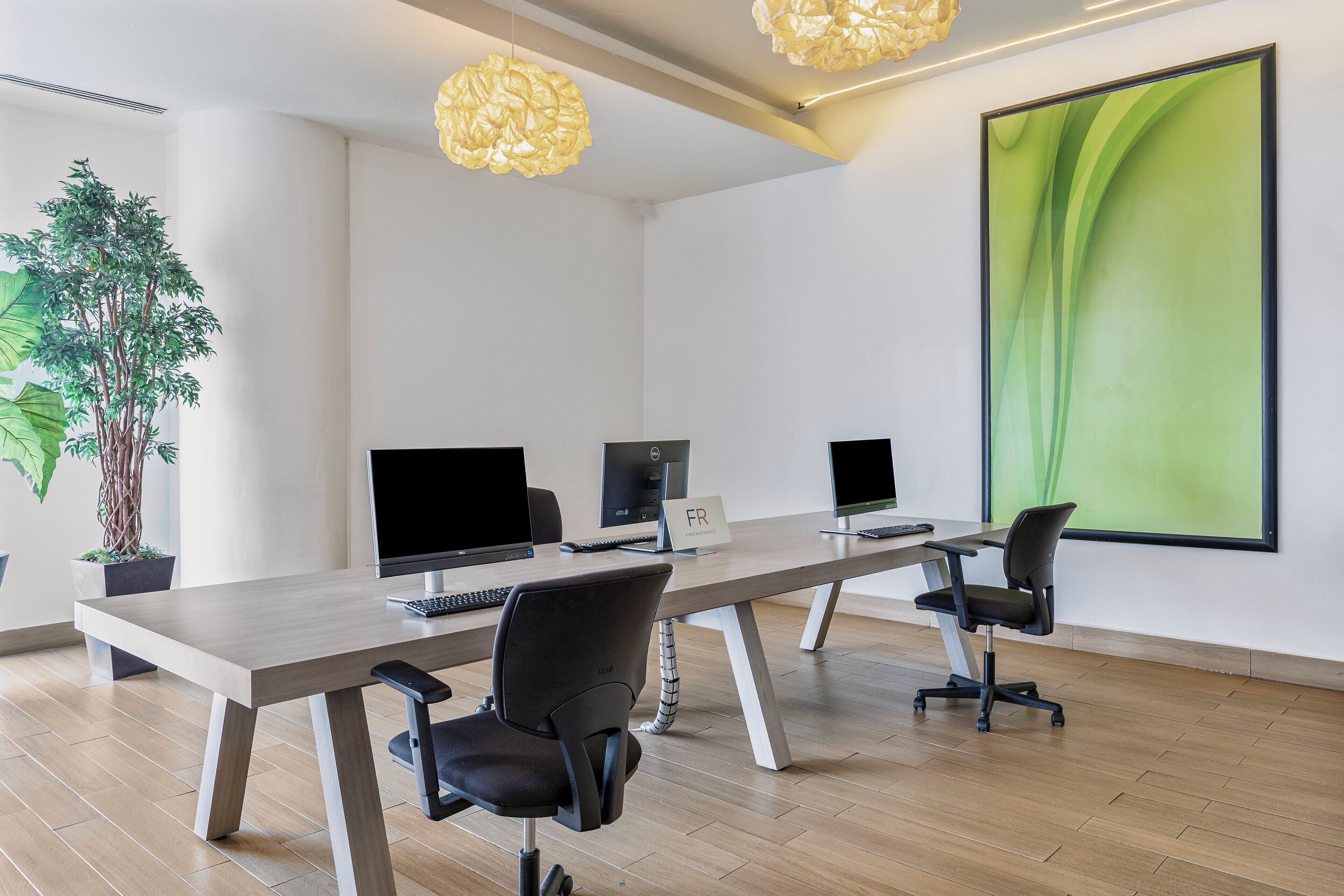 A modern conference room with a long table, four chairs, and three computer monitors.