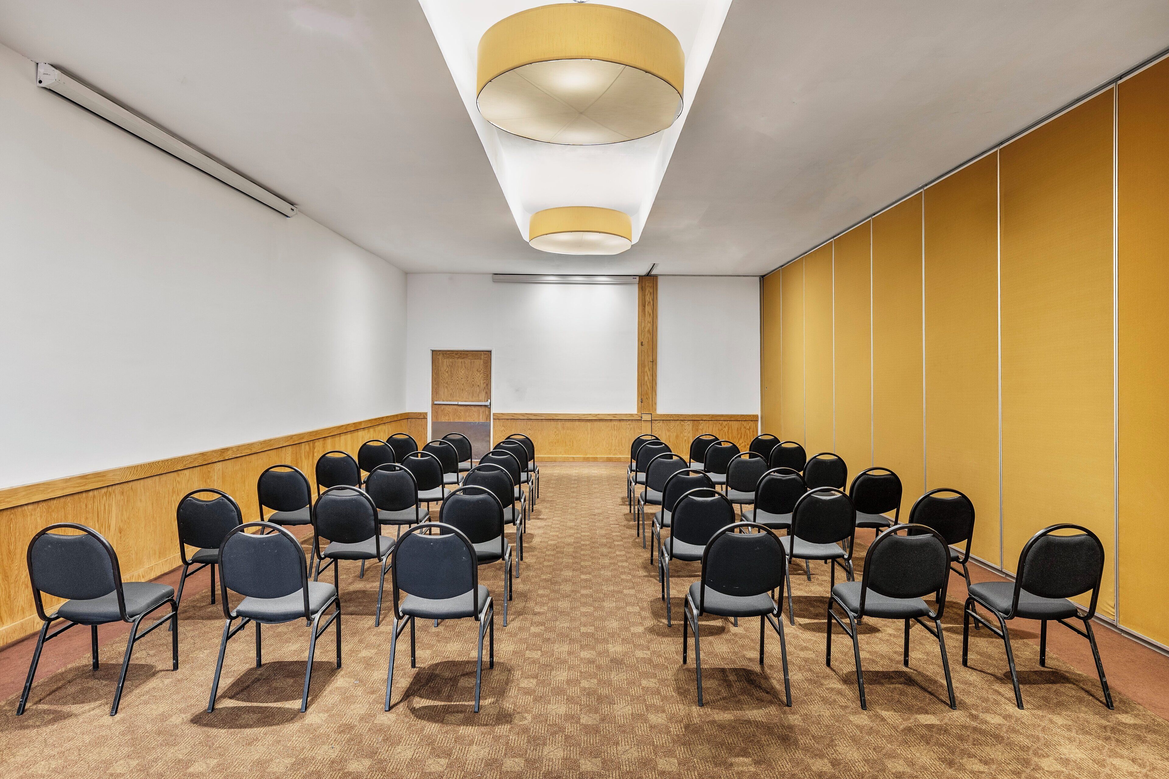 A conference room with rows of chairs, a wooden panel wall, and a ceiling light fixture.