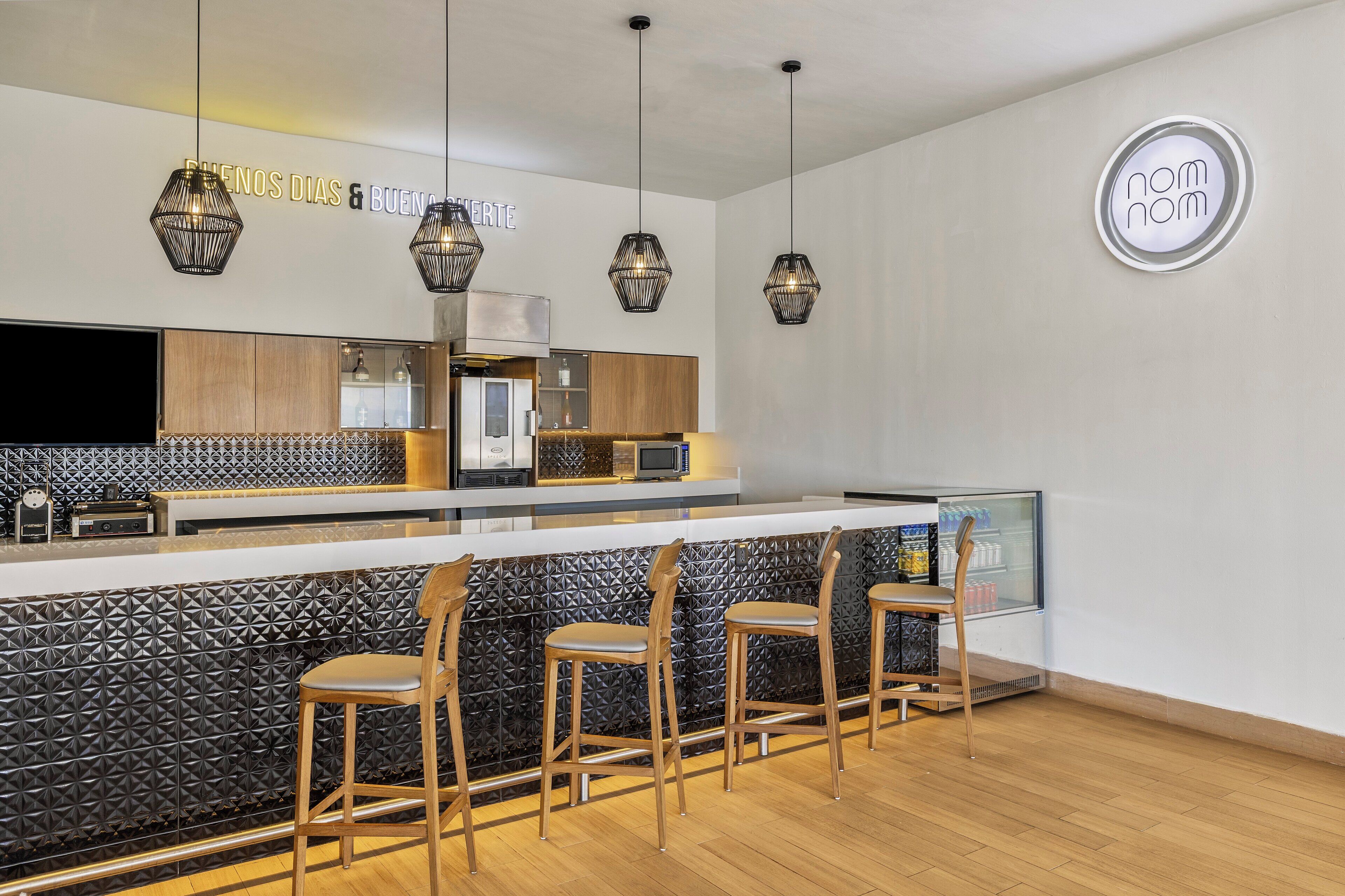 Cocina moderna con barra, destacando un protector contra salpicaduras negro con textura, taburetes de madera y lámparas colgantes.