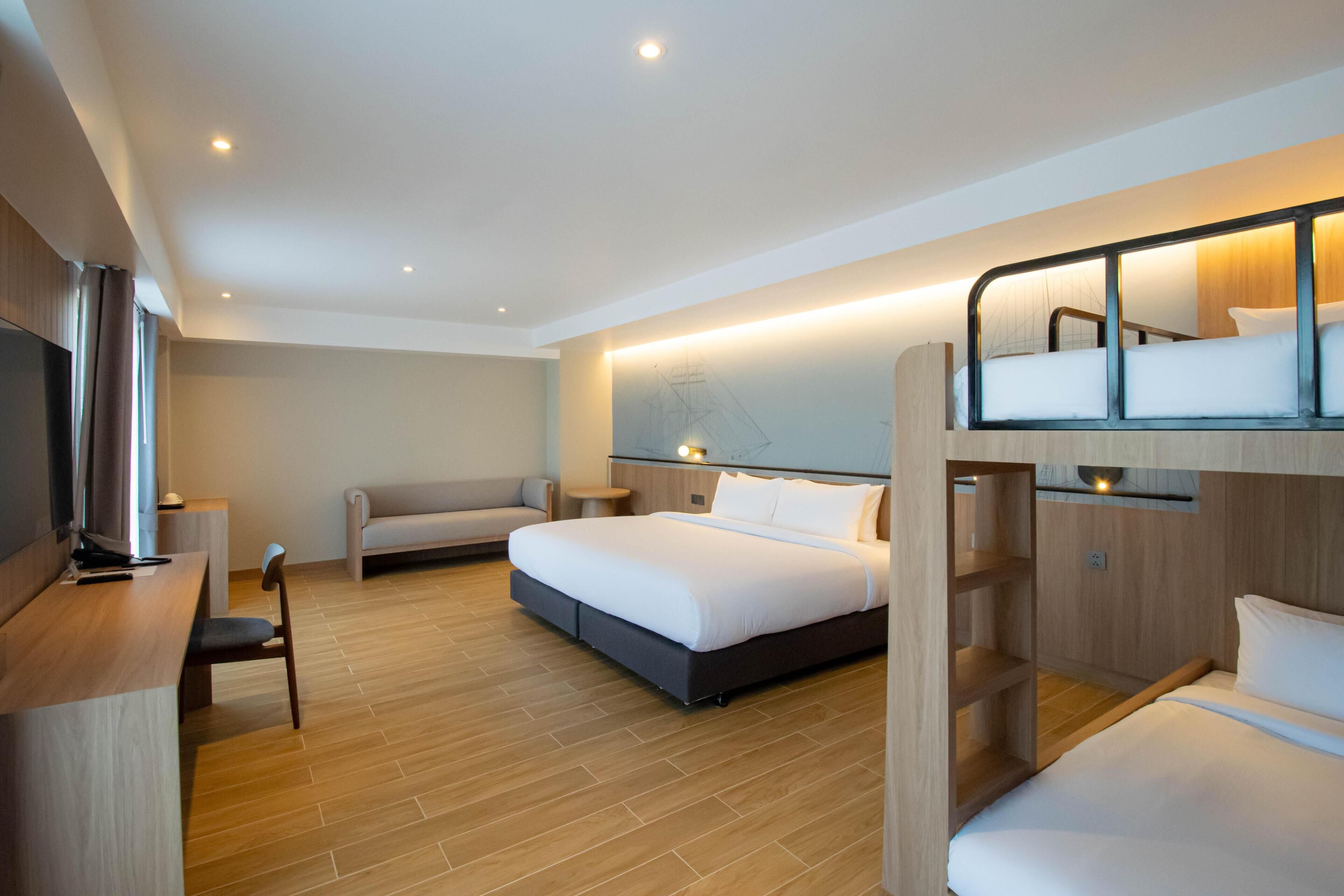 A modern hotel room with a bunk bed, a desk with a chair, a sofa, and a television.
