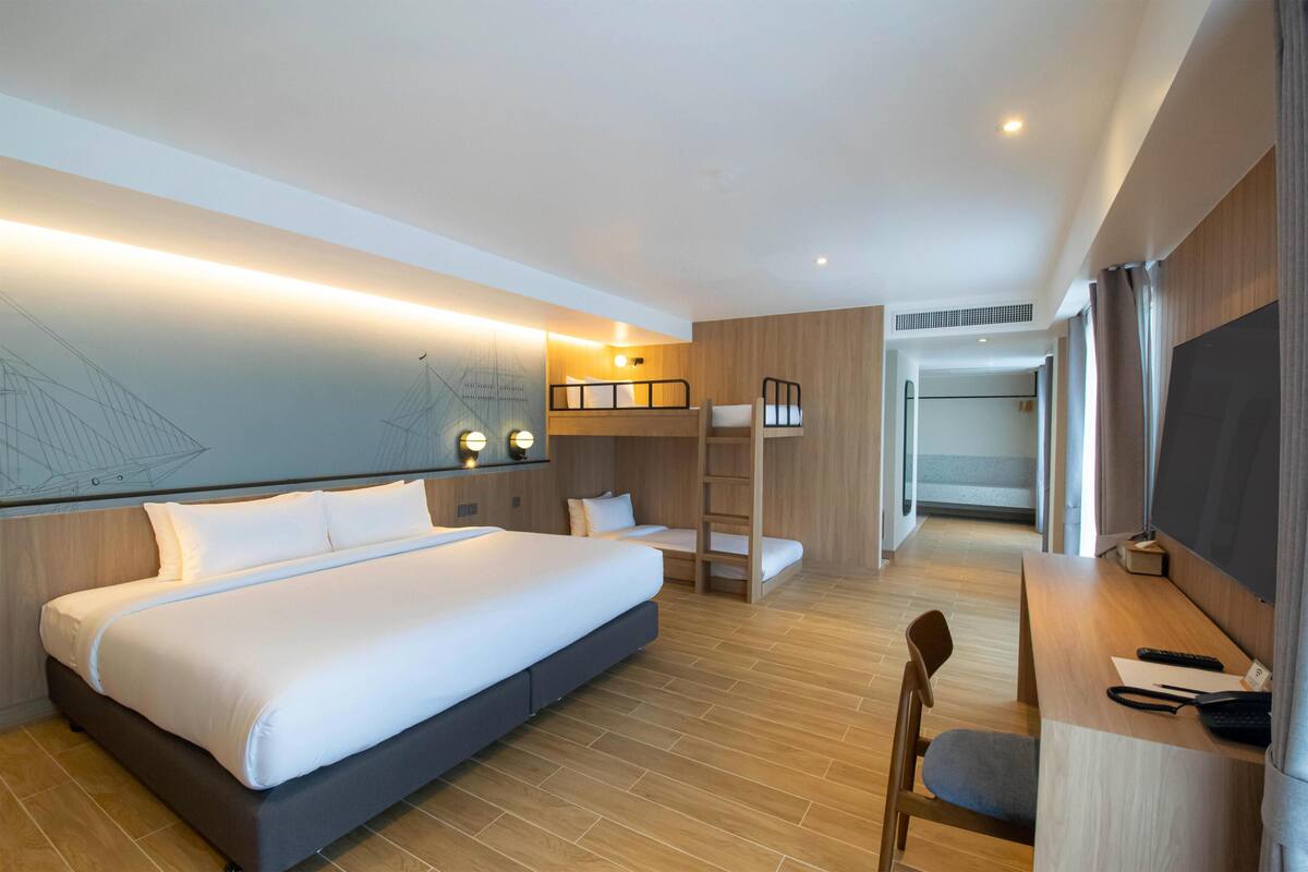 Een moderne hotelkamer met een groot bed, een bureau met stoel, een stapelbed en een televisie.