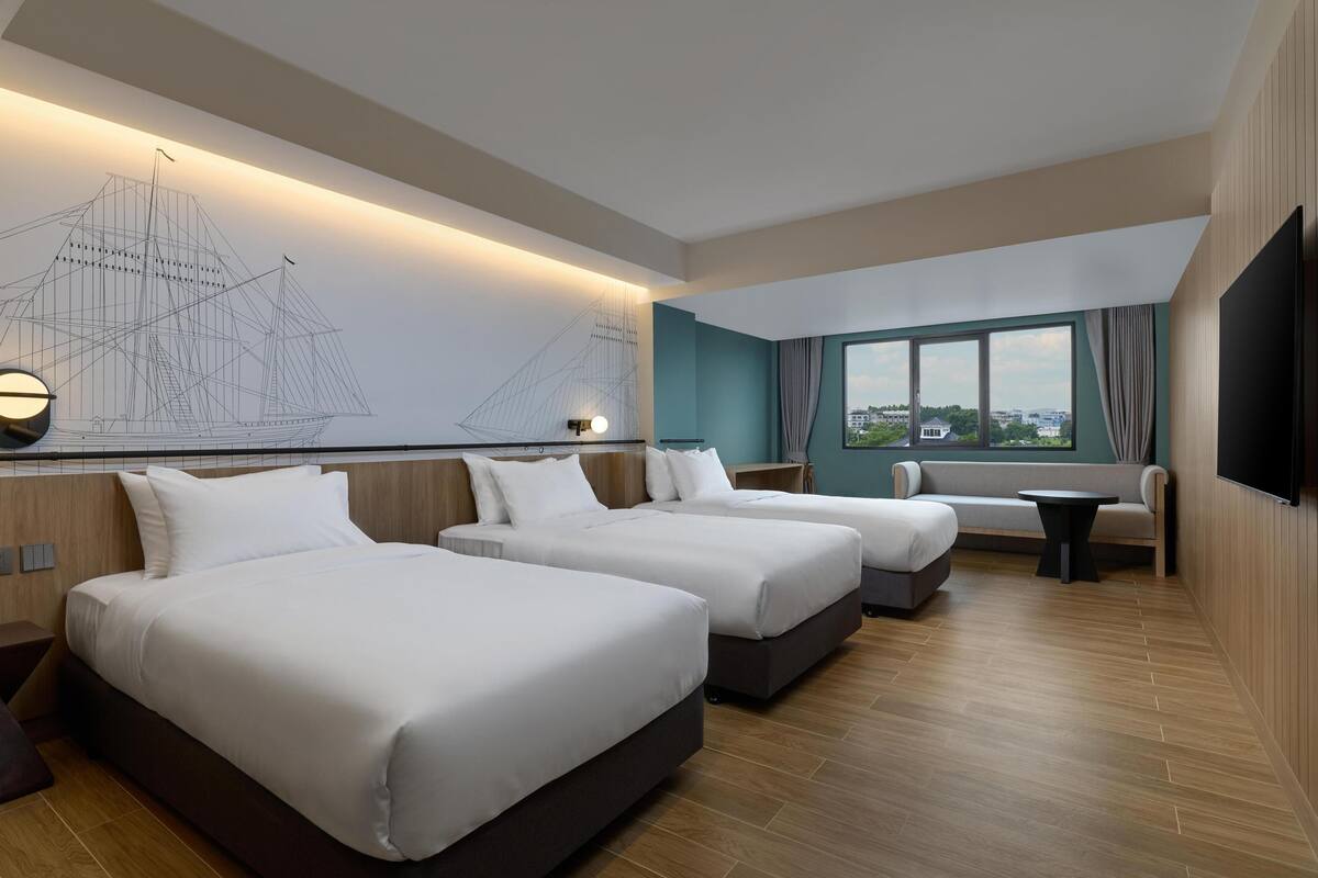 Een hotelkamer met drie bedden, een groot raam met uitzicht, een tv aan de muur en een zithoek met een tafel.
