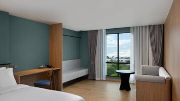 A modern hotel room with a bed, a desk, a chair, a small table, and a balcony with curtains.