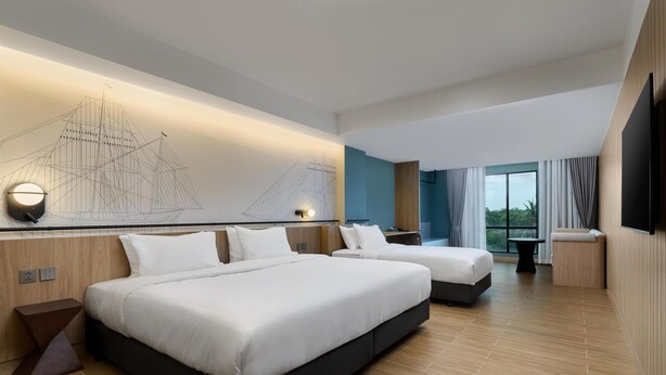 Una habitación de hotel moderna con dos camas, un ventanal con cortinas, una obra de arte en la pared con un barco, y un televisor de pantalla plana.