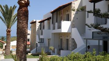 A modern multi-story building with balconies, a garden area, and a clear view of the sea.