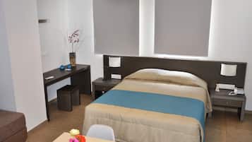 Une chambre d’hôtel avec un lit, un bureau, une chaise et une petite table sur laquelle est posé un vase de fleurs.
