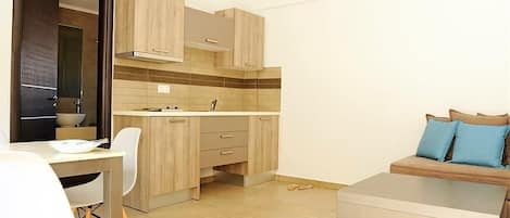 A compact kitchen with wooden cabinets, a dining area with white chairs, and a sofa with blue cushions.