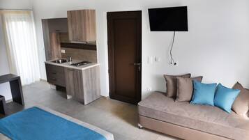 Una habitación de hotel moderna con kitchenette, un sofá con cojines azules y un televisor de pantalla plana montado en la pared.
