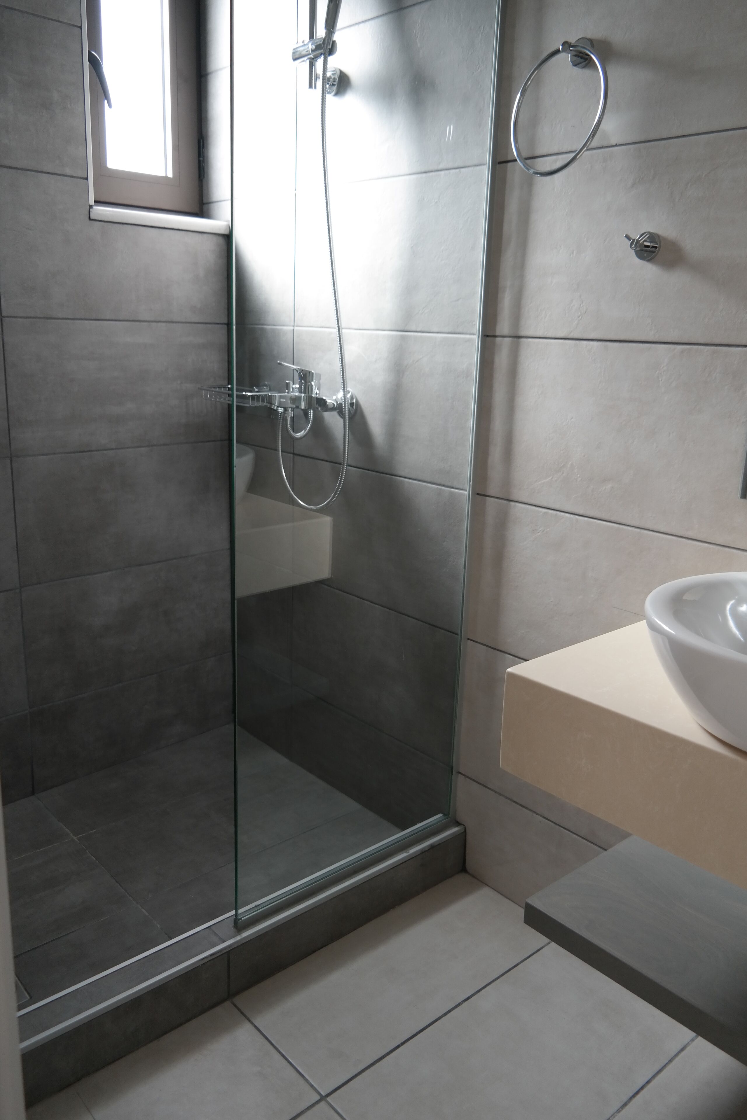 A modern bathroom with a glass-enclosed shower, a white sink, and a small mirror.