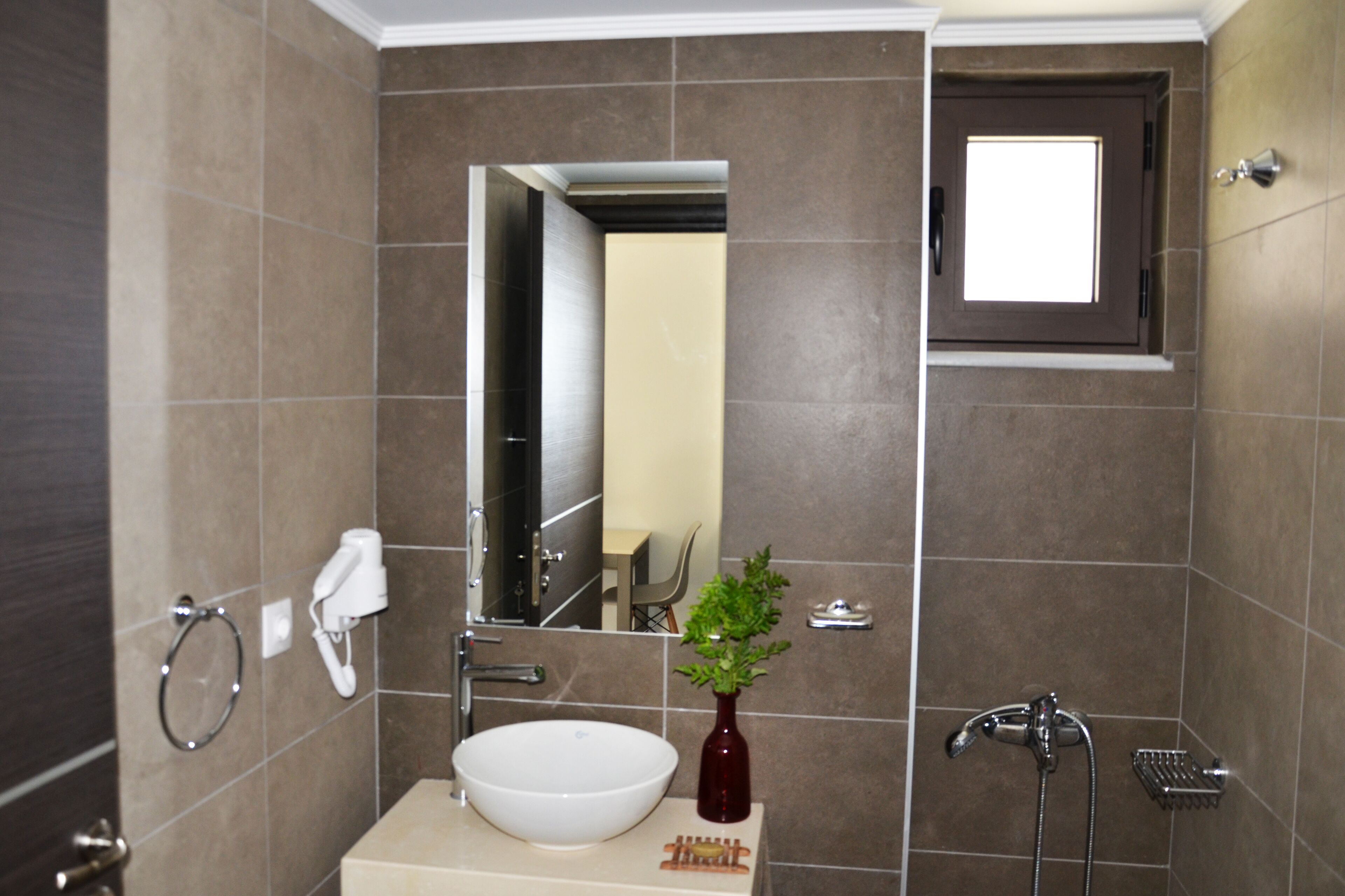 Een badkamer met een wit wastafelmeubel, een spiegel, een handdoekhouder, een klein plantje en een douche.