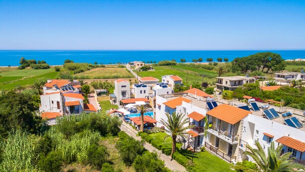 Un quartier résidentiel situé sur la côte, avec des maisons dotées de toits couverts de tuiles rouges, de panneaux solaires et offrant une vue sur la mer.