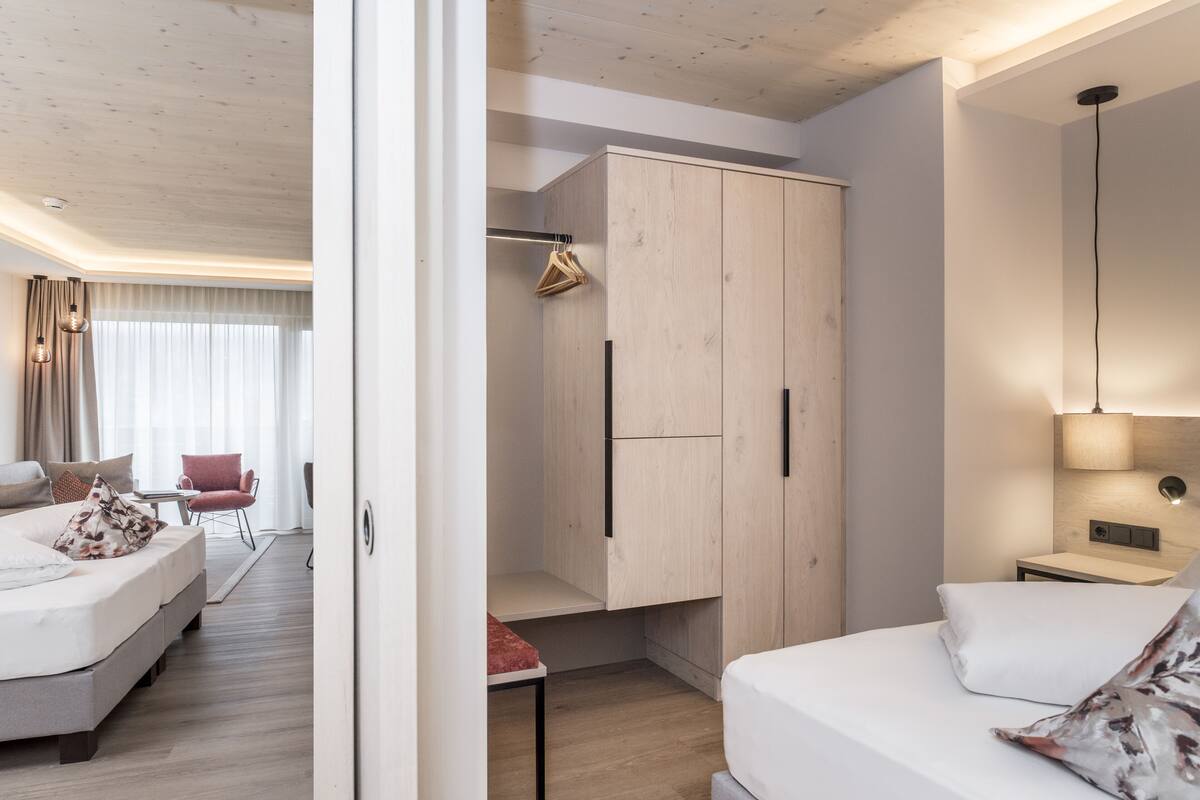 Quarto de hotel moderno com uma cama, área de estar com uma poltrona, guarda-roupa e mesa de cabeceira.