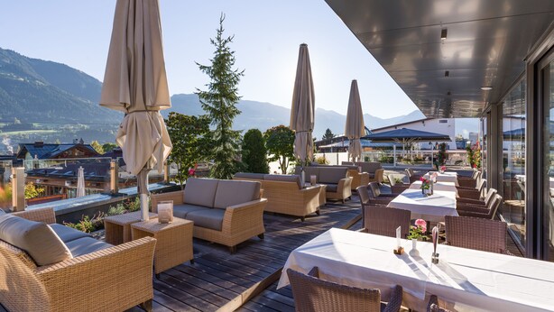 A terrace with wicker furniture, umbrellas, and a view of mountains. - Aktiv Hotel Schweizerhof - Kitzbühel (Kitzbuhel)