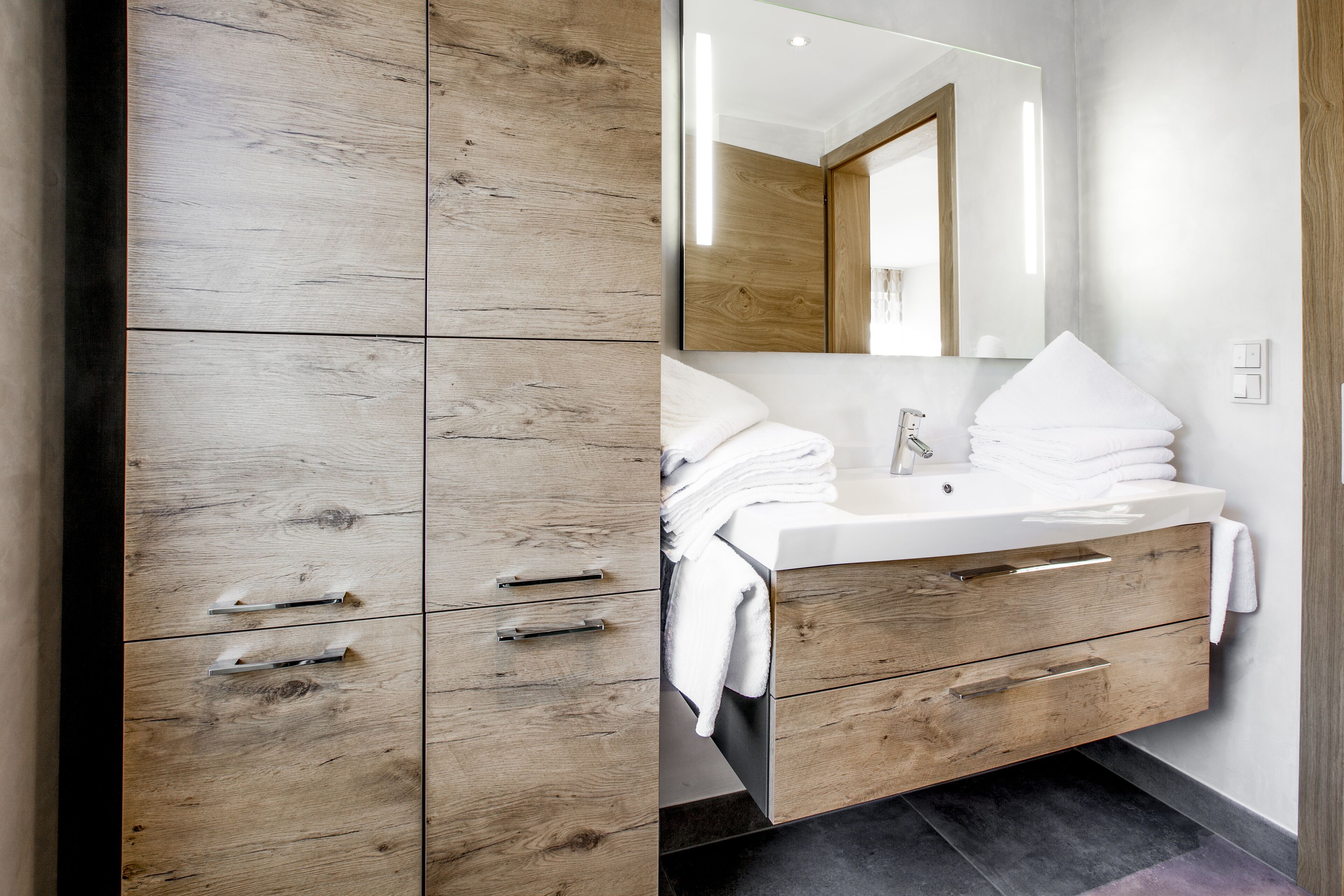 A modern bathroom with a wooden vanity, a sink, and a mirror.