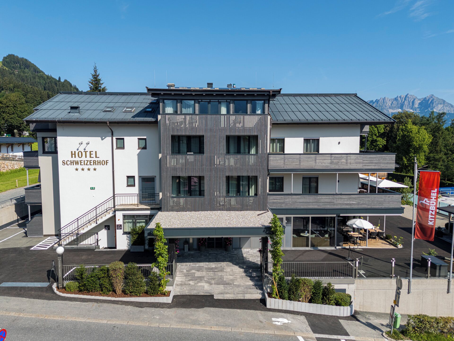 Un hotel moderno con techo plano, una escalera que conduce a la entrada y un cartel que indica que es el Hotel Schweizerhof.