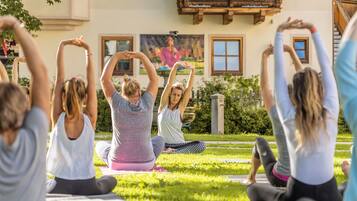Un grupo de personas practicando yoga al aire libre en un área con césped, con un edificio en el fondo.