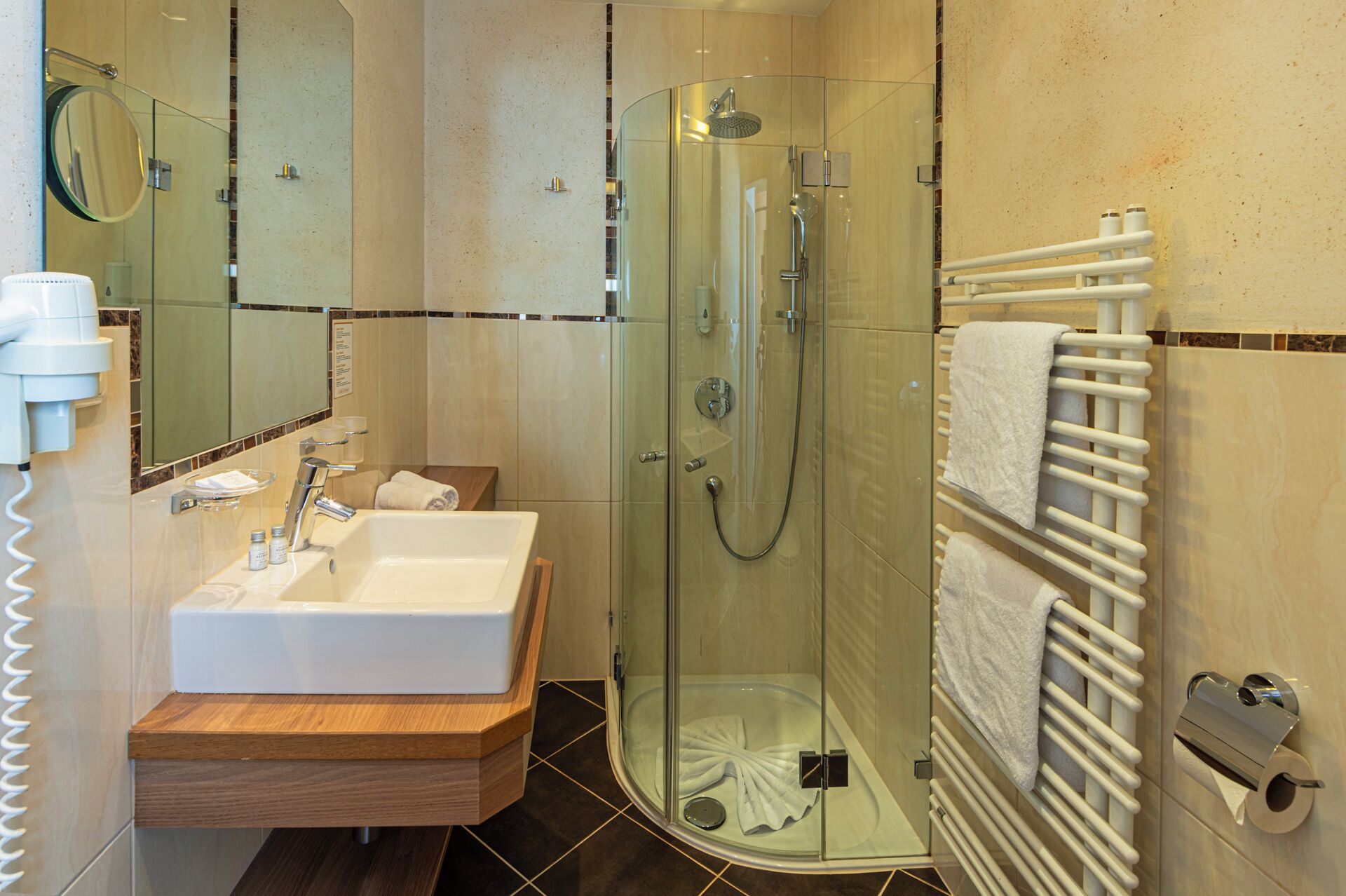 Ein modernes Badezimmer mit einer gläsernen Duschkabine, einem Waschbecken mit Holzschublade und einem Handtuchhalter.