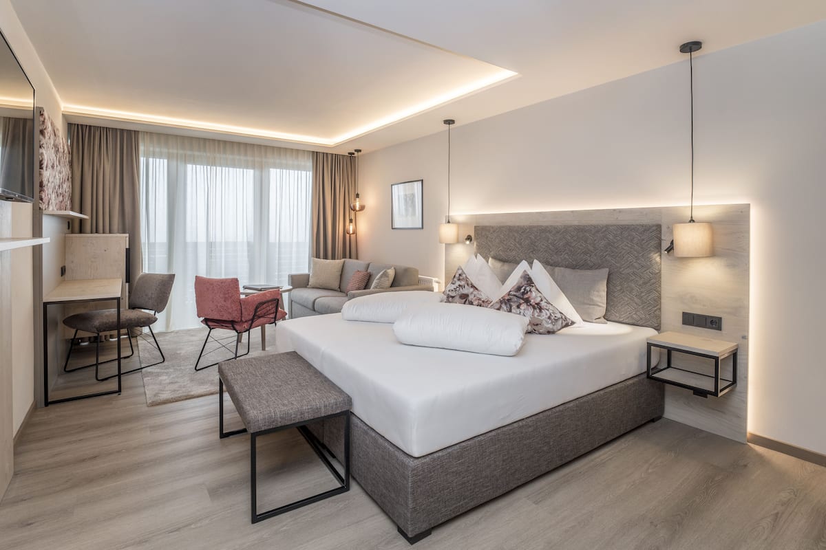 Quarto de hotel moderno com uma cama grande, uma escrivaninha, uma cadeira e um sofá.
