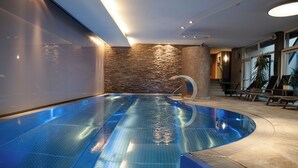 A modern indoor swimming pool with a stone wall and a curved design. - Aktiv Hotel Schweizerhof - Kitzbühel (Kitzbuhel)