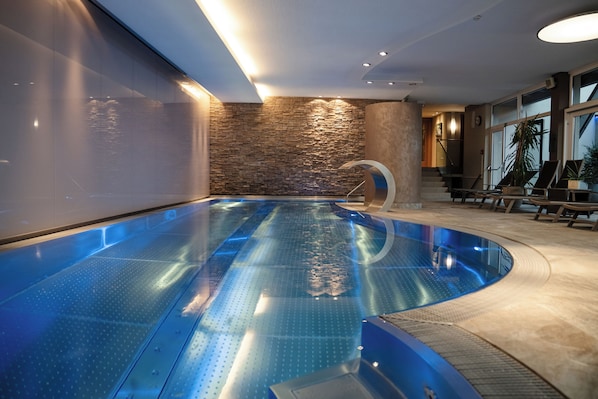 A modern indoor swimming pool with a stone wall and a curved design.